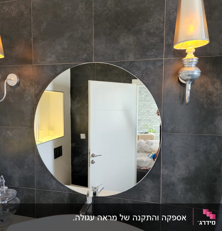 מראה עגולה תלויה על קיר כהה בחדר אמבטיה